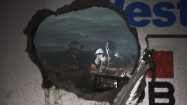 Workers peer though a hole created by a boring machine where two sections of tunnel meet below Concord.