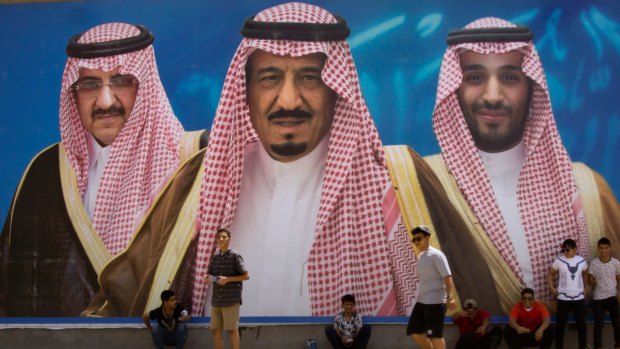 Saudi boys pose in front of a huge billboard showing in the centre, King Salman, with his 31-year-old son Mohammed bin Salman to the right, and Prince Mohammed bin Nayef to the left.