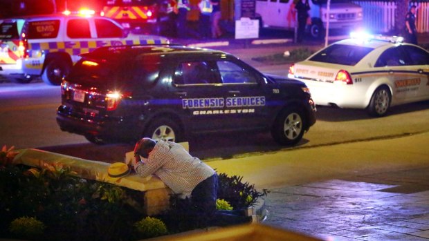 A man kneels across the street from where police gather outside the Emanuel AME Church following a shooting Wednesday.