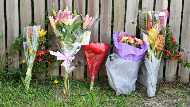 Flowers against a fence across the road from the scene of the multiple stabbing in Manoora.