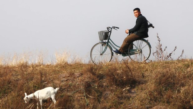 With a gun on his shoulder, a young North Korean man on a bicycle watches a Chinese tourist boat passing by in Sinuiju on the North Korean side of the Chinese border.