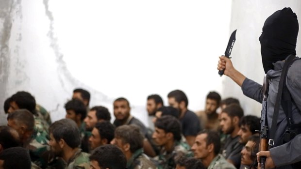 An image from the Raqqa Media Centre, shows a fighter from the Islamic State group, armed with a knife and an automatic weapon, next to captured Syrian army soldiers and officers, in Raqqa, Syria, last year. 