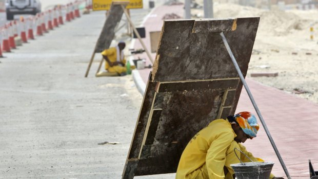 An Asian labourer avoids the direct sun by using the shade of a wooden sign as he works on a manhole beside a road under construction in Dubai, United Arab Emirates. 