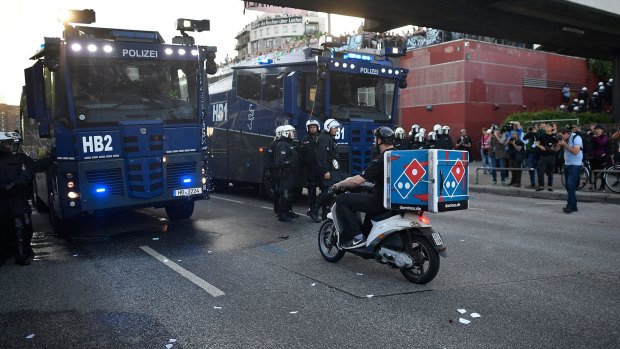 HAMBURG, GERMANY - JULY 06: A pizza delivery man rides a scooter towards police vehicles during the "Welcome to Hell" protest march on July 6, 2017 in Hamburg, Germany. Leaders of the G20 group of nations are arriving in Hamburg today for the July 7-8 economic summit and authorities are bracing for large-scale and disruptive protest efforts tonight at the "Welcome to Hell" anti-G20 protest. (Photo by Alexander Koerner/Getty Images)