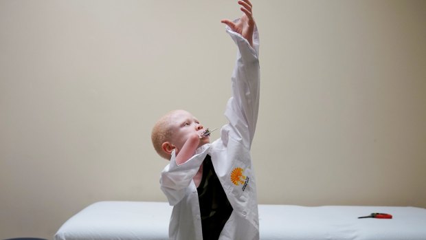 Baraka Lusambo, 7, puts on his shirt during a prosthetic fitting while he sucks on a lollipop in hospital in Philadelphia.