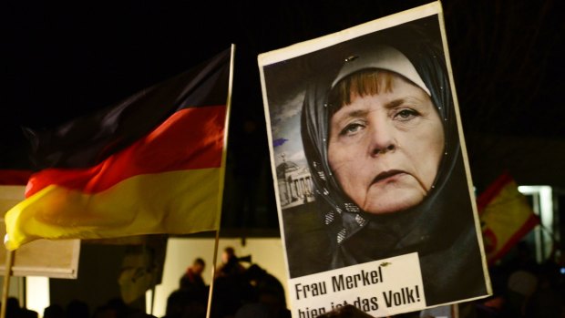 A protester in Dresden in 2015 holds a poster of German Chancellor Angela Merkel wearing an Islamic headscarf in front of a Reichstag building with a crescent on top.