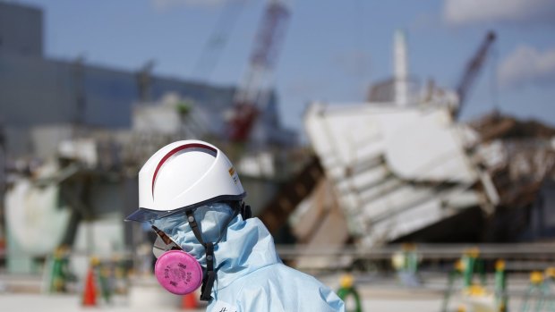 A Tokyo Electric Power Co. employee, wearing a protective suit and a mask, walks in front of the No.1 reactor building at the tsunami-crippled Fukushima Dai-ichi nuclear power plant in Okuma earlier this month.