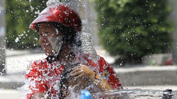 A woman and a girl riding on a motorbike react as a boy splashes water on them during traditional Thai New Year celebrations or Songkran water festival in Bangkok.