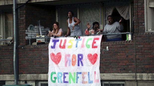 People watch from a balcony as people walk during a demonstration following the fire at Grenfell Towers.