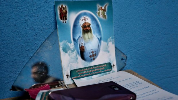 A Christian man, reflected in a mirror, sits near a photo of priest who was killed by IS militants.