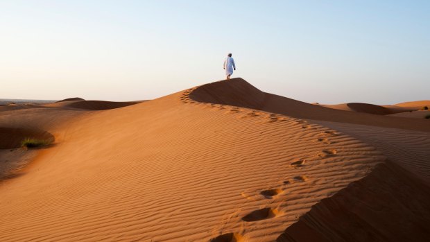 A lone figure walks a sand dune ridge at sunset. 