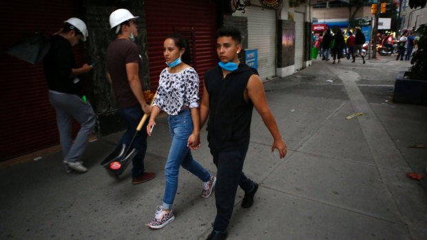 A young couple, dust masks pulled down, hold hands as they walk down a street in the Condesa neighbourhood. Residents are roaming the streets looking for ways to help in the earthquake rescue and recovery effort.