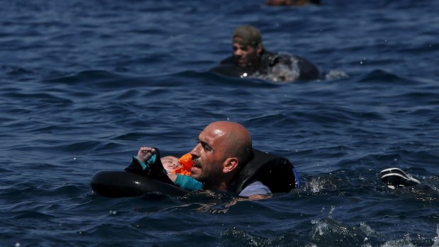 A Syrian father holding a baby in a lifetube swims towards the shore after their dinghy deflated some 100m away before reaching the Greek island of Lesbos.