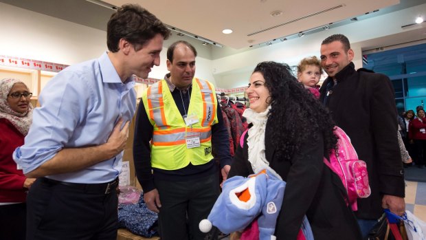Prime Minister Justin Trudeau, left, greets Georgina Zires, center, Madeleine Jamkossia and her family, refugees fleeing from Syria, as they arrive at Pearson International airport, in Toronto on December 11, 2015. 