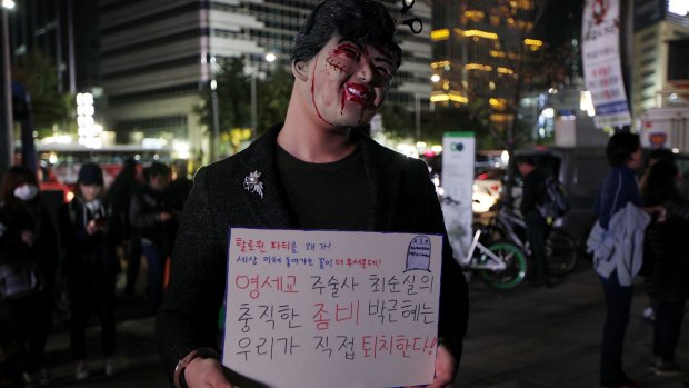 A protester in Seoul sports a Halloween-influenced mask of   President Park Geun-Hye.  The placard reads: "Why do you need Halloween fest? We can see all the horror in our lives."