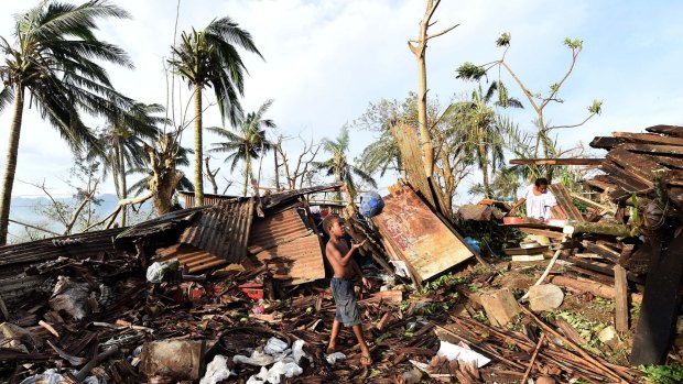 A boy plays with a ball as his mother searches through the ruins of their family home in Port Vila, Vanuatu. 
