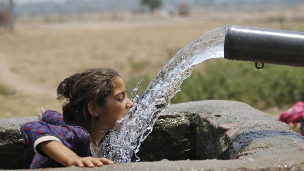A girl drinks water from an irrigation tube in northern India's Jammu region during a May heatwave.