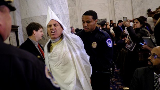 Code Pink activist Tighe Barry, dressed like a member of the KKK, is removed by police officers after disrupting the start of the Senate Judiciary Committee confirmation hearing for Senator Jeff Sessions.