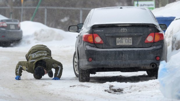 A police officer looks for evidence under a car in the area of a Quebec City mosque.