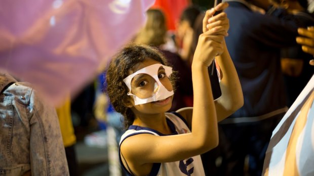 A child holds a flag as she wears a paper mask during a march against Brazil's President Michel Temer in Rio de Janeiro.