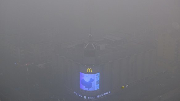 A video display on the side of a building shows a map of China amid heavy pollution and fog in Beijing.