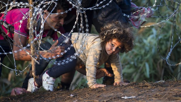 A child is helped to cross from Serbia to Hungary through the barbed wire fence near Roszke.