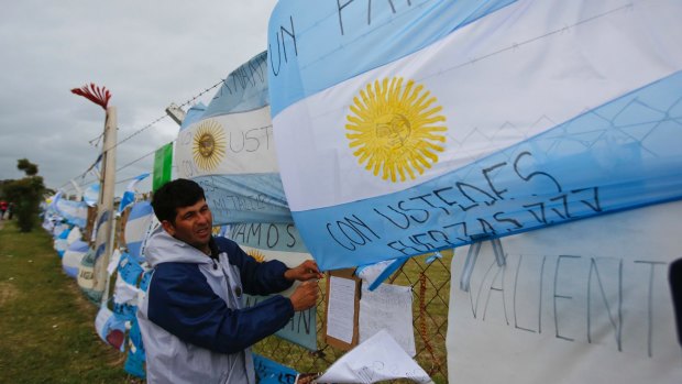 A man ties an Argentine flag to a fence at the Mar de Plata Naval Base.