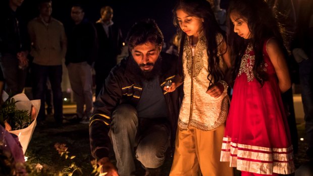 Adnan Amjid, a friend and housemate of Zeeshan Akbar, helps girls light candles at a vigil outside a Caltex service station in Queanbeyan where the 29-year-old Caltex attendant was fatally stabbed.