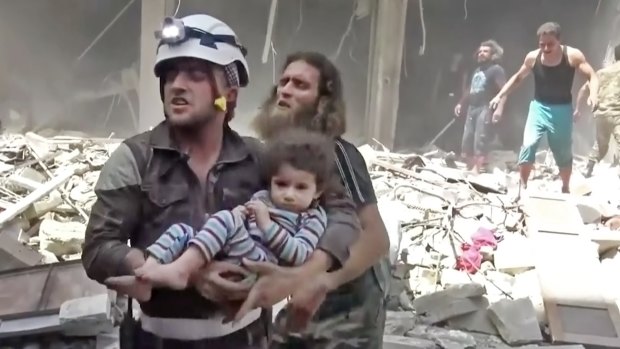 In this image made from video and posted online, a Civil Defence worker carries a child after air strikes hit Aleppo, Syria, in April.