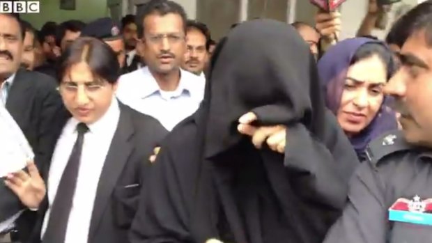 Ayyan Ali covers her face as she tries to avoid the media while being taken to a police van.