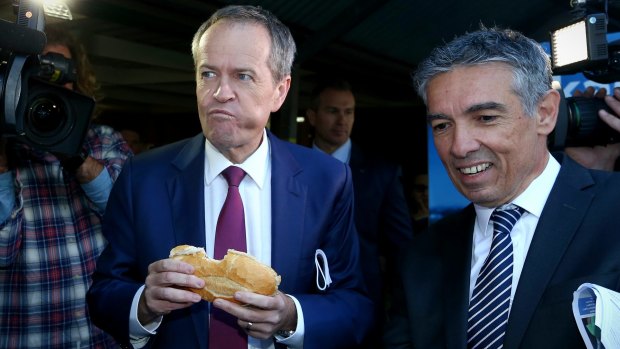 Opposition Leader Bill Shorten eats a sausage together with the ALP candidate for Reid, Angelo Tsirekas, during a visit to a polling booth on Saturday.
