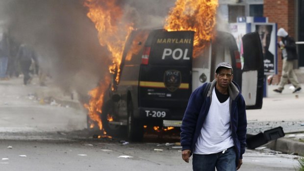 A man walks past a burning police vehicle, during unrest following the funeral of Freddie Gray in Baltimore.