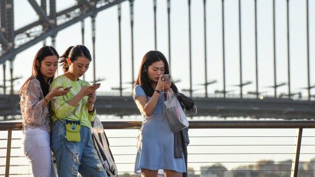 People using mobile phones around the Opera House precinct.  Advertisers are now putting their ads on the pavement as an increasing number of people are looking down as they walk while using their smartphones. 