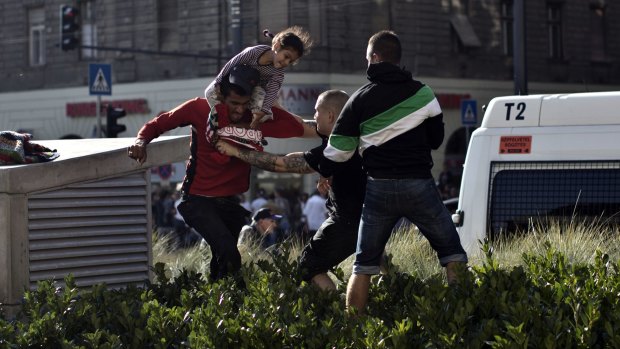 A Syrian man carrying a child scuffles with a Hungarian nationalist in front of Keleti train station in Budapest.