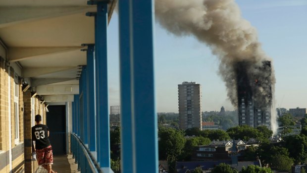 A resident in a nearby building watches smoke rise from the tower on fire in London.