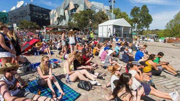 Fans settle in at Federation Square to watch the grand final in the sun.