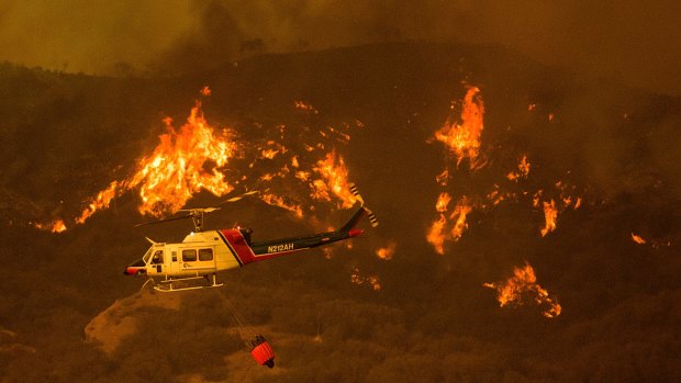 A helicopter carries water while trying to keep a wildfire from jumping Santa Ana Road, near Ventura, California on Saturday.