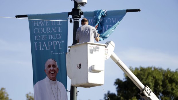 A worker hangs banners ahead of Pope Francis' scheduled visit on the Benjamin Franklin Parkway in Philadelphia. 