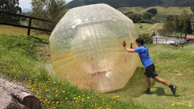 A man pushes his friend up a hill in a Zorb ball.