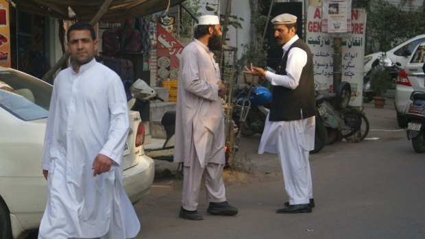 A man wearing the Afghan hat known as a pakol, right, speaks in the streets of Delhi's Little Kabul.