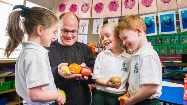 Farrer PS kindergarten students Elsa Connell, Grace Evans and Oliver Turnbull talk to Acting ACT Chief Health Officer Dr Andrew Pengilley about fruit while learning about good nutrition as part of a new school curriculum. 