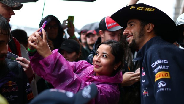 Daniel Ricciardo poses for photographs with fans in pit lane.
