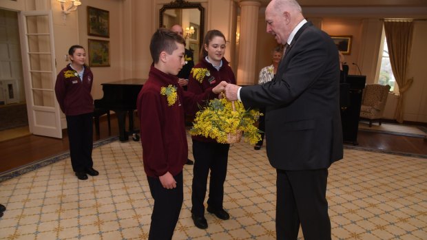 Governor-General Sir Peter Cosgrove receives a basket of wattle from Holy Spirit Primary School Nicholls students Aiden Monteleone and Holly Fahy to mark Wattle Day on Thursday, September 1.