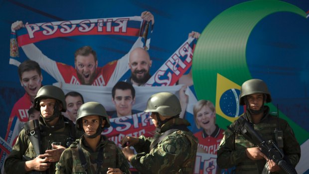 Soldiers stand in front of a wall decorated with photographs showing fans and athletes of the Russian team.