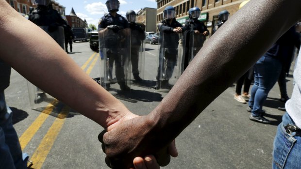 Members of the community hold hands in front of police officers in riot gear outside a recently looted and burned CVS store in Baltimore, Maryland.