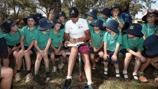 Former prime minister Tony Abbott presents a signed copy of his book <i>Battlelines</i> to students of Caragabal Public School.