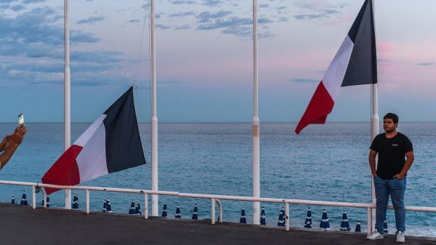 A man poses for a picture next to French flags flying at half mast on the Promenade des Anglais in Nice, France.