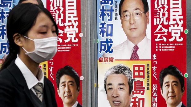 Shinzo Abe's smile is on display as a woman in Tokyo walks past election posters for Japan's snap election.