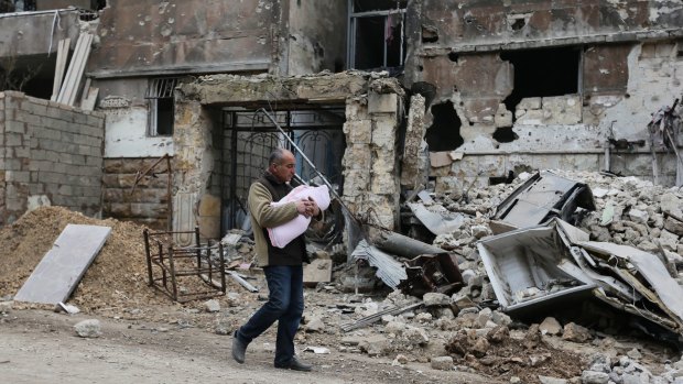 A man carries a baby as he walks past rubble in the once rebel-held Salaheddine neighbourhood of Aleppo.