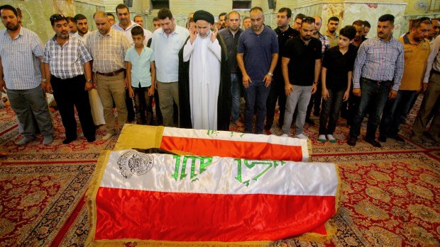 Mourners pray in front of the Iraqi flag-draped coffins of two bombing victims.